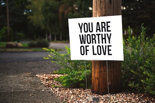 A positive message sign "You are worthy of love" in a park setting.